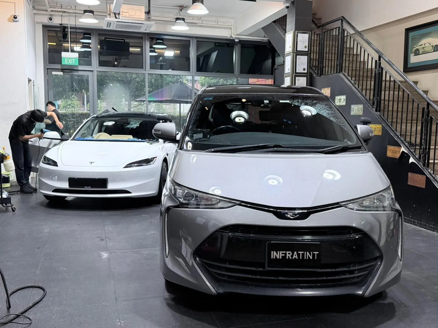 A grey SUV with large kidney grille and a white car behind it in a workshop.