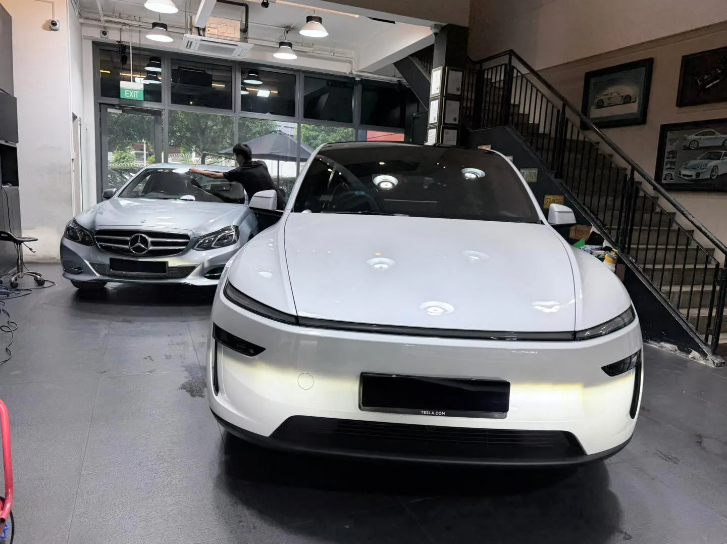 A grey sedan with visible window tinting being applied in the workshop.