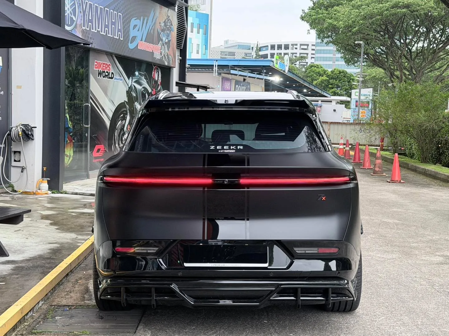 A dark SUV with red rear light strip, parked at a public charging point, viewed from the rear.