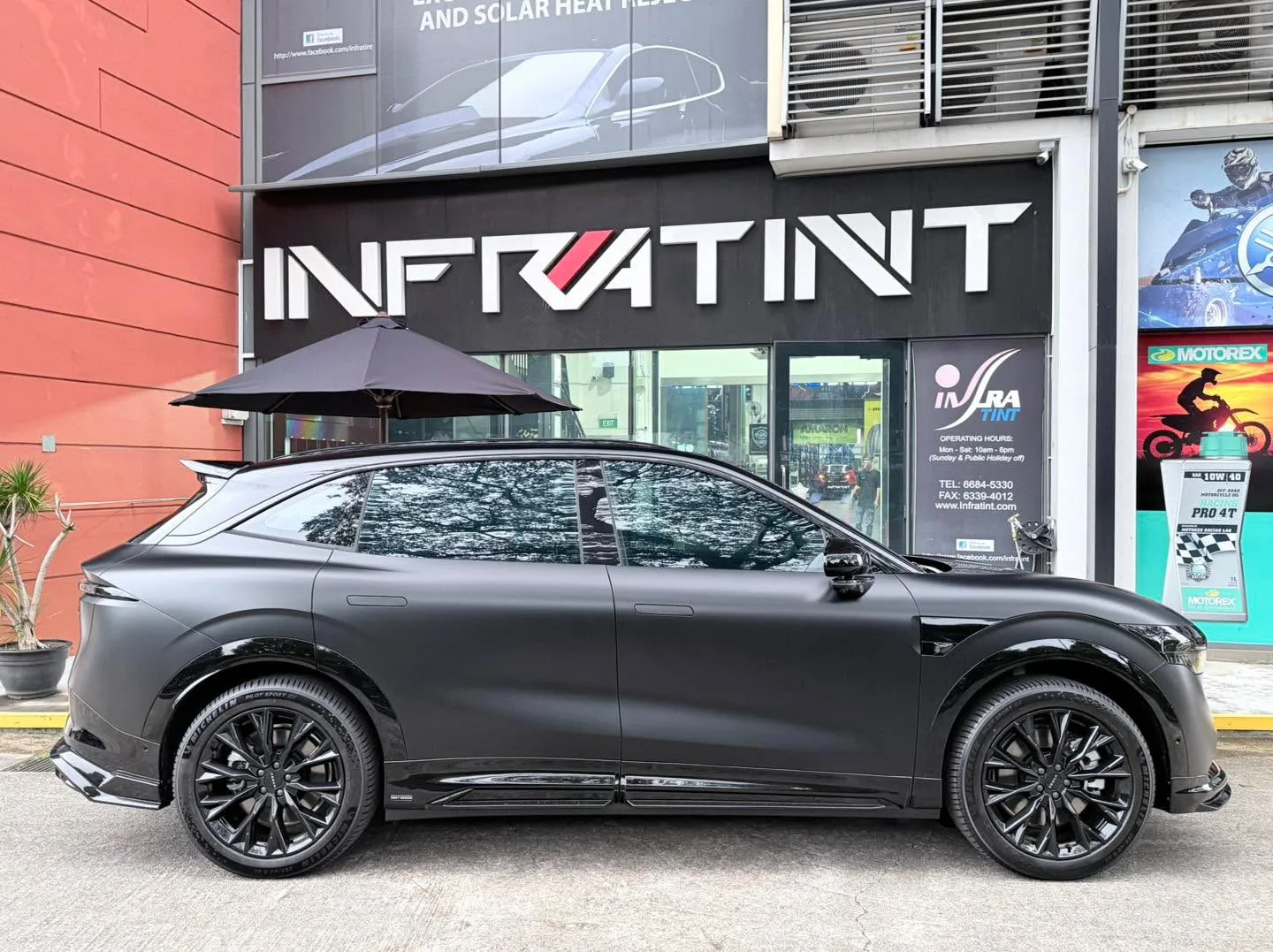 A gunmetal grey SUV with black alloy wheels parked outside the Infratint workshop, viewed from the side.