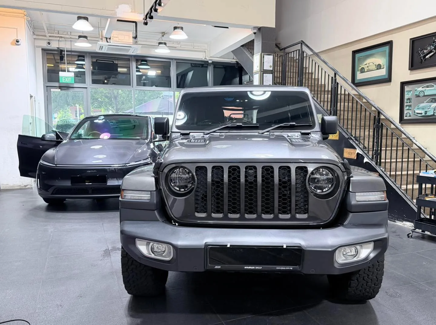 A dark grey Jeep SUV with distinctive round headlights and open bonnet, viewed head-on indoors.