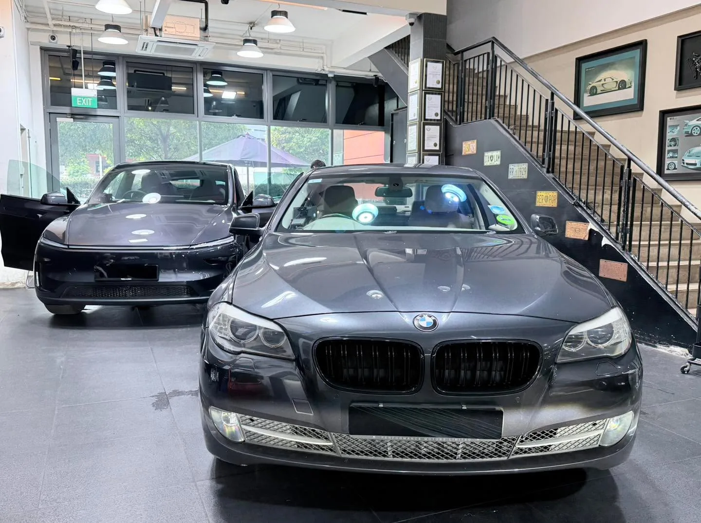 A black sedan with rainbow-tinted windscreen and a dark Mercedes-Benz behind it.