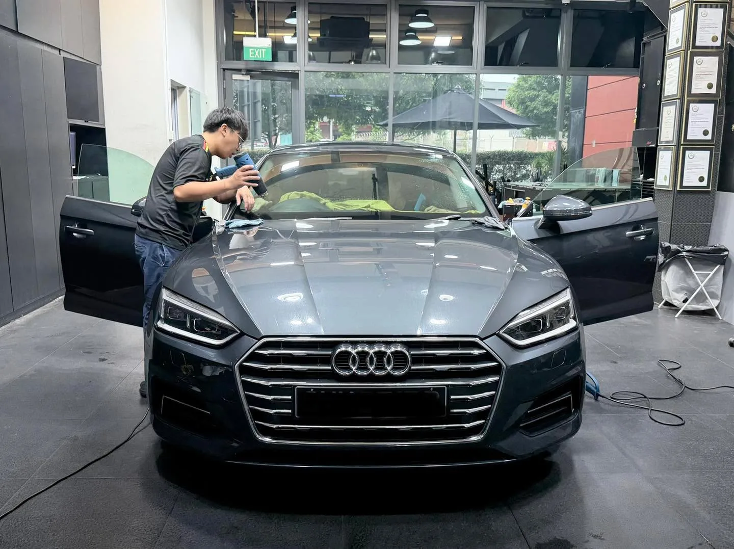 A dark sedan with open doors being worked on by technicians, rainbow tint visible on windscreen.