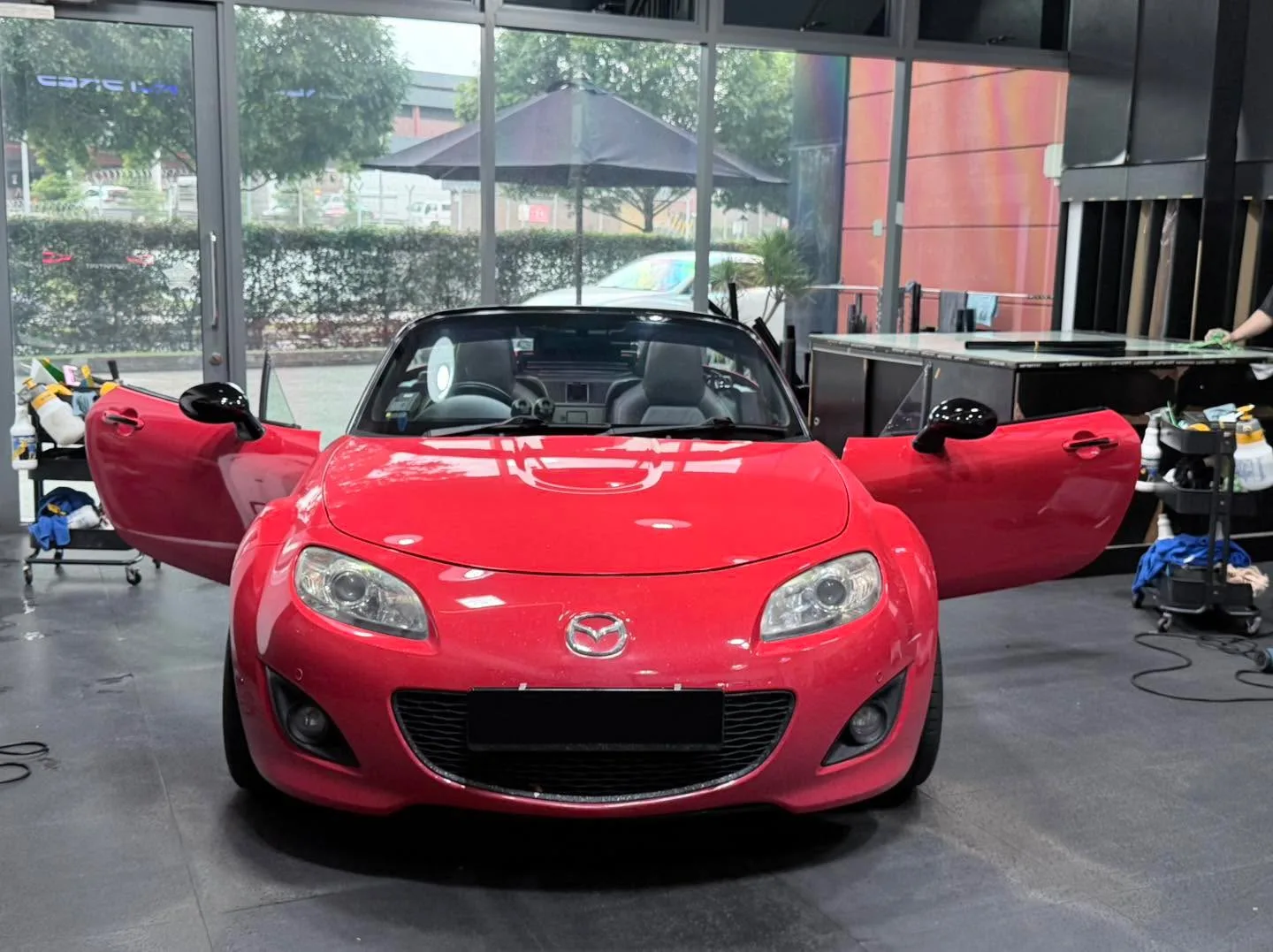 A bright red Mazda MX-5 convertible with doors open in the workshop.
