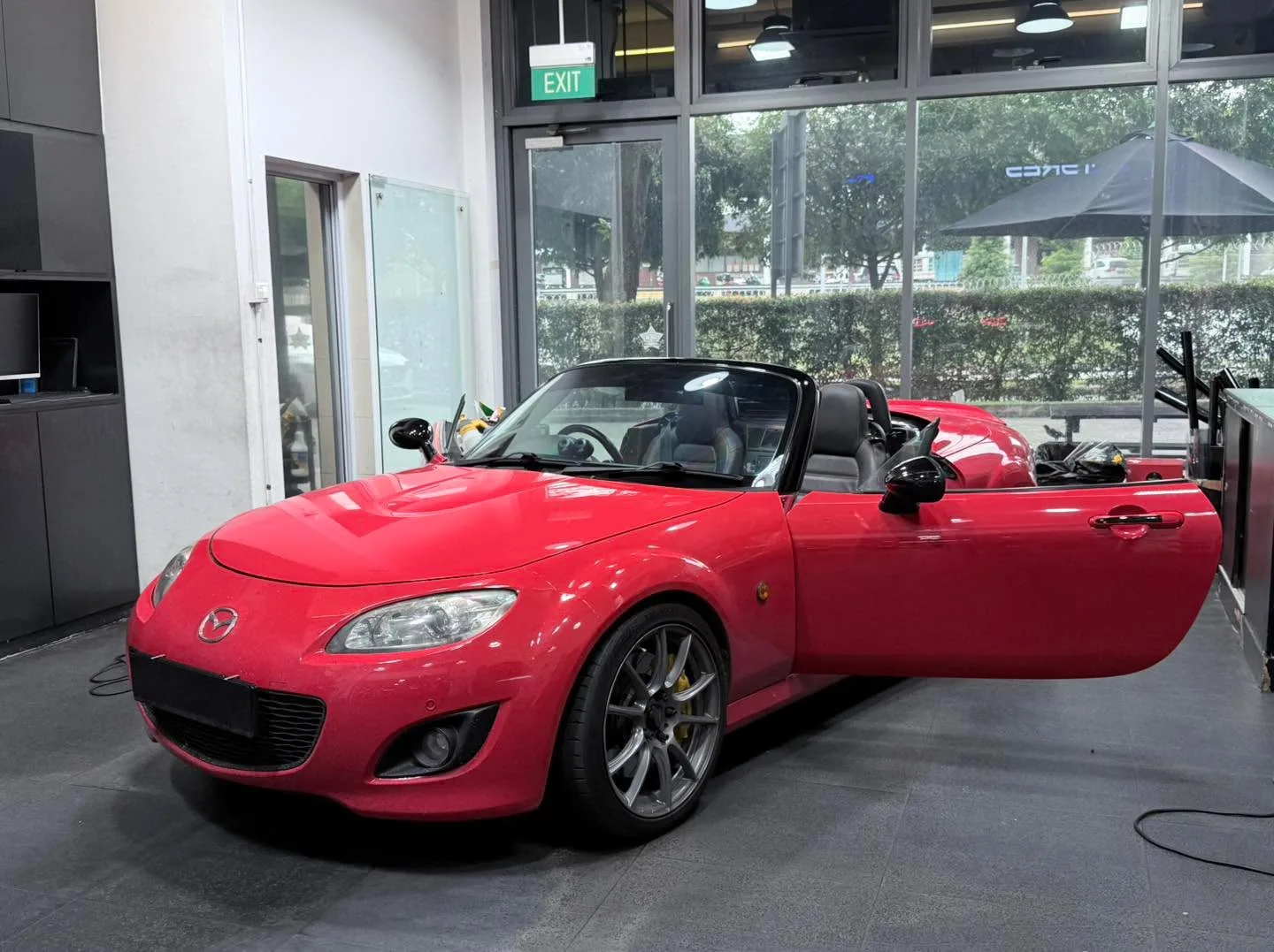 A bright red Mazda MX-5 roadster with door open, parked indoors.
