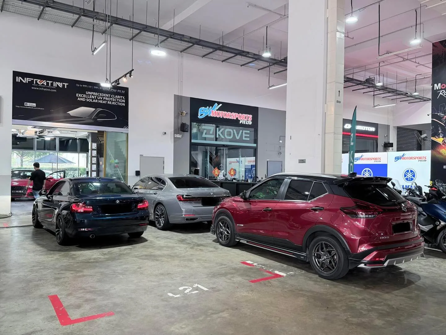 Three cars parked in a tinting workshop: a dark blue saloon on the left, a silver sedan in the centre and a burgundy SUV on the right.