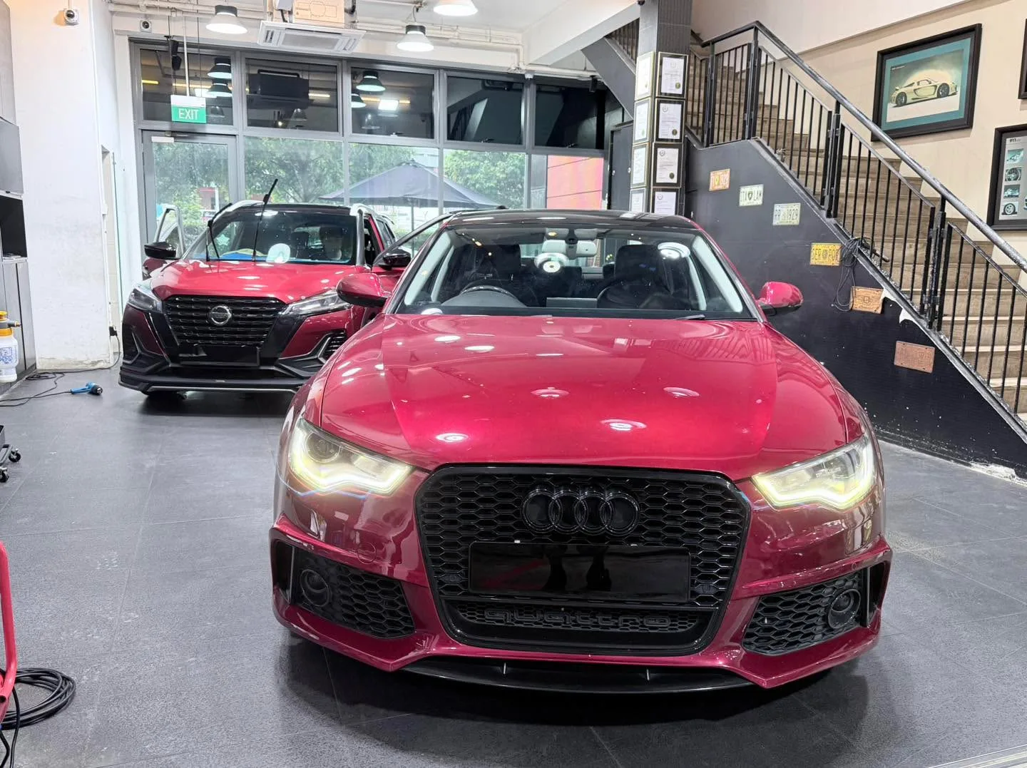 A burgundy saloon faces the camera in an indoor workshop, with a dark red SUV visible behind it.