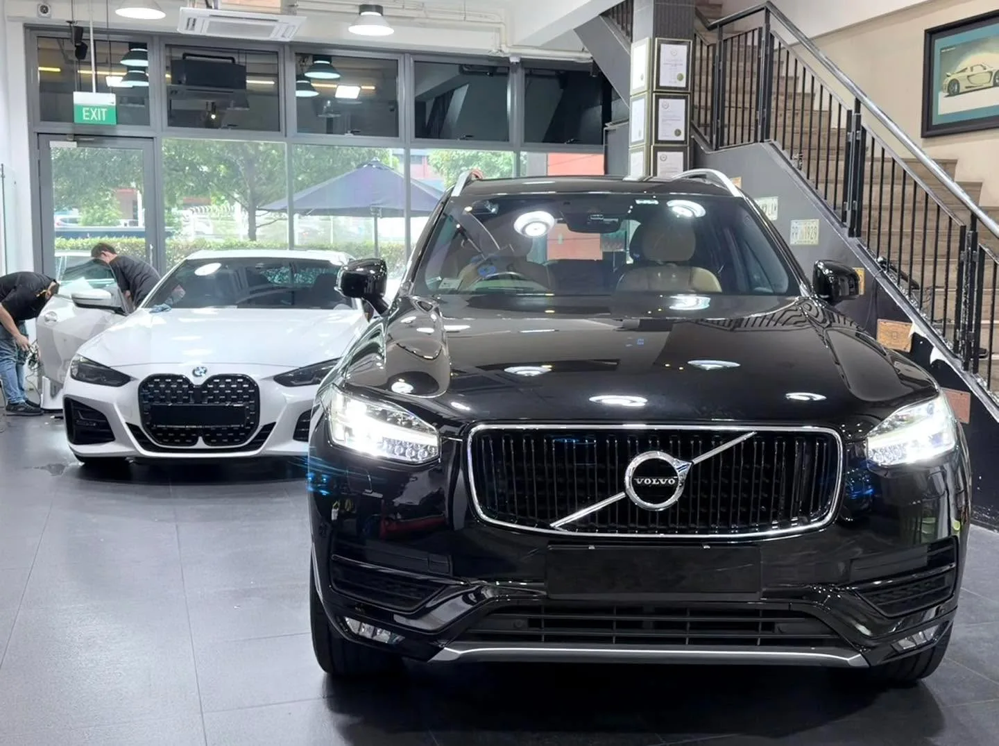 A white BMW saloon and a black Volvo SUV facing the camera in an indoor workshop.