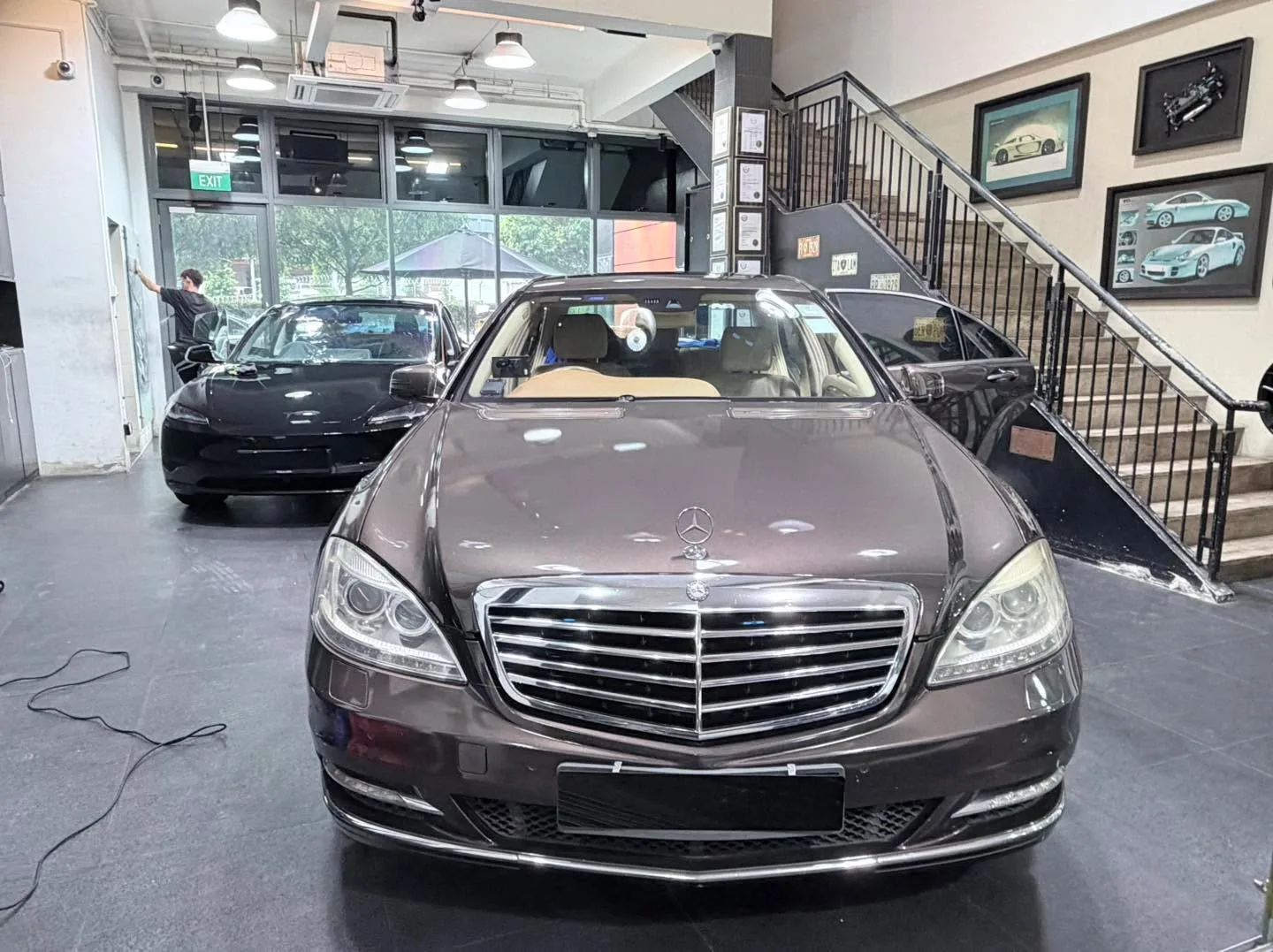 A dark Mercedes-Benz saloon positioned centrally in a workshop with a staircase behind it.