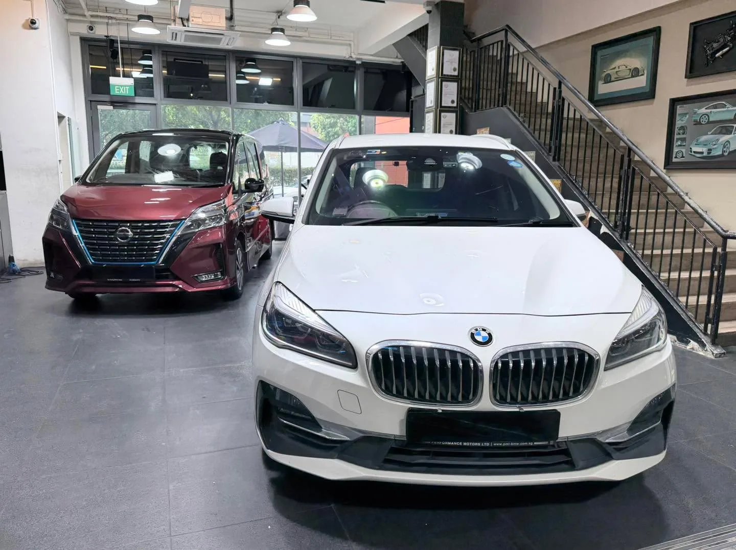 A white BMW saloon and a burgundy Nissan MPV side by side on a workshop floor.