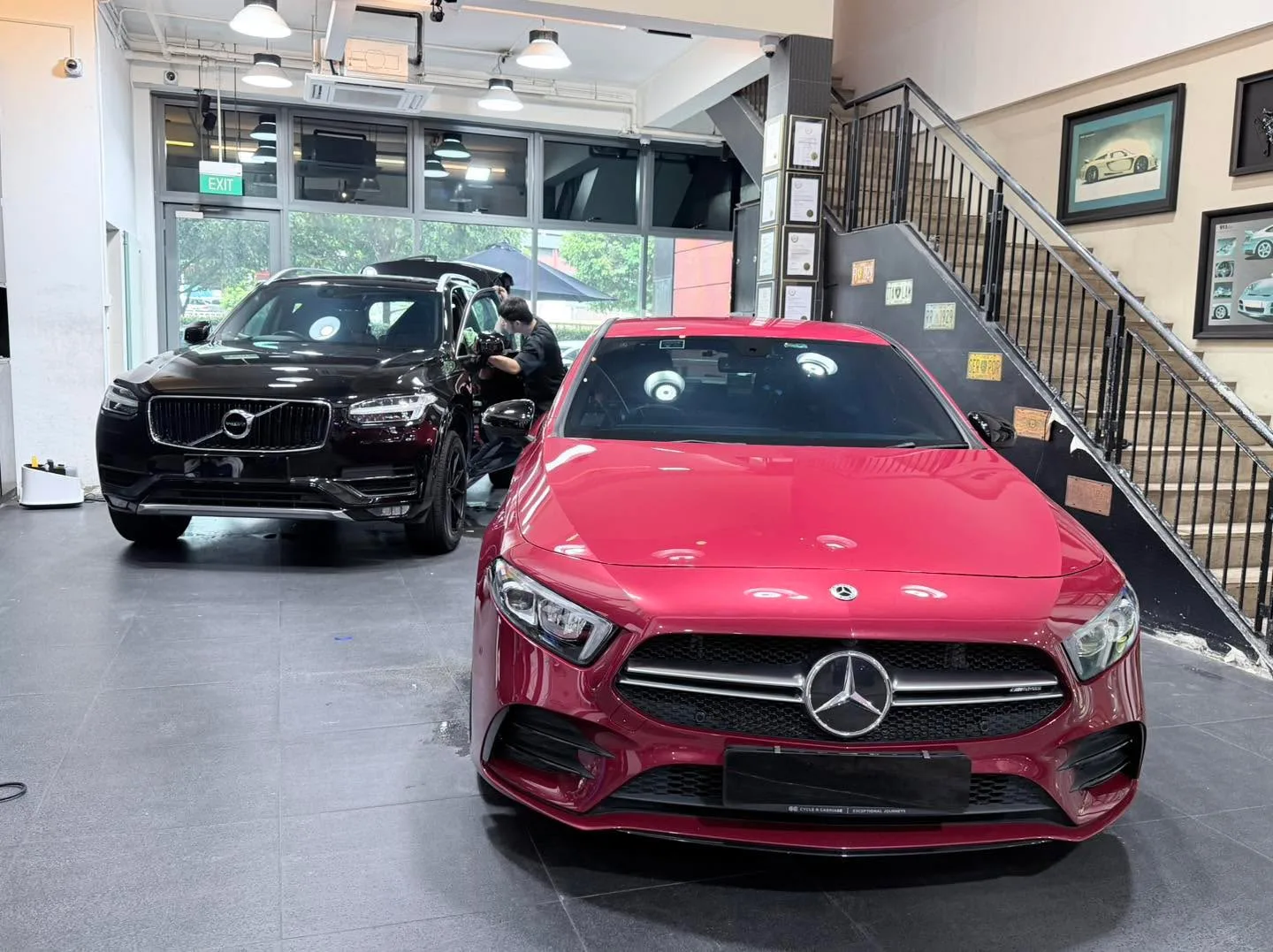 A black Volvo SUV and a burgundy Mercedes-Benz saloon positioned in a workshop.
