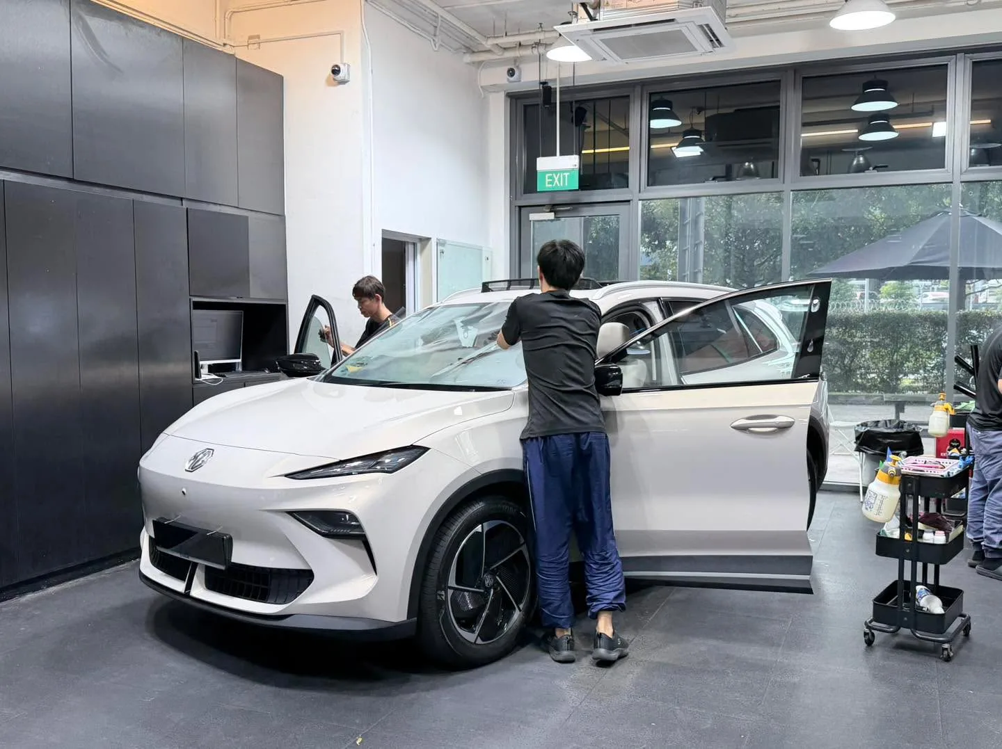 A white Tesla with its door open as a technician applies window film inside the workshop.
