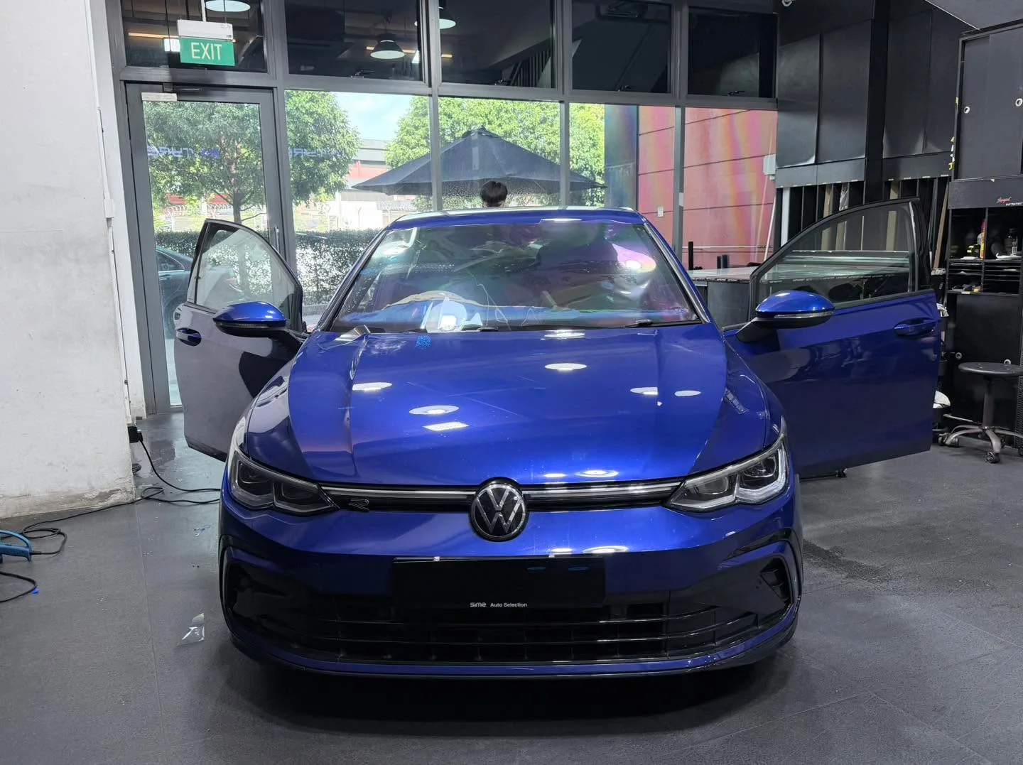 A bright blue Volkswagen Golf facing forward with both doors open in a workshop.