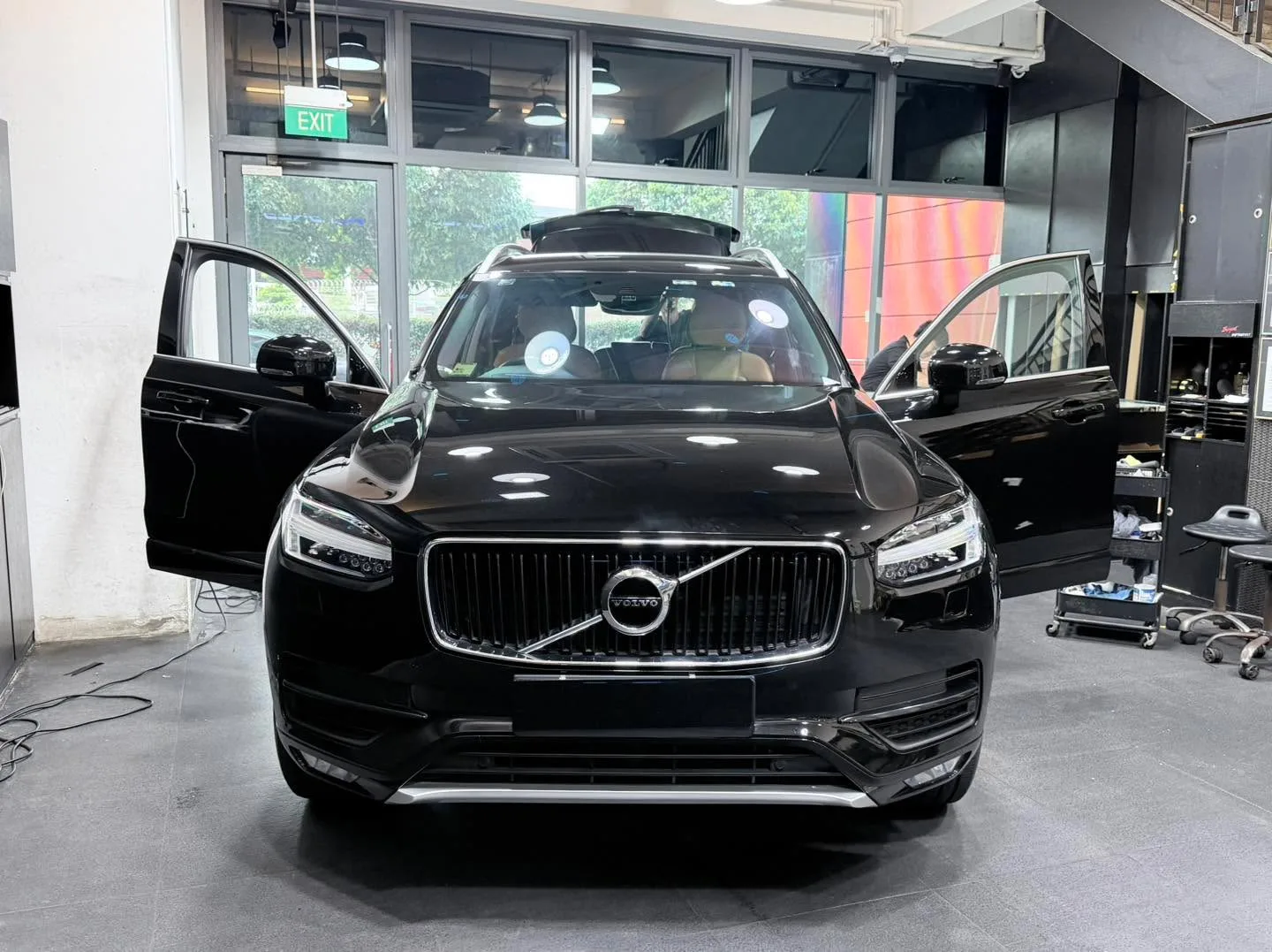 A black Volvo SUV positioned with both front doors open in a workshop setting.