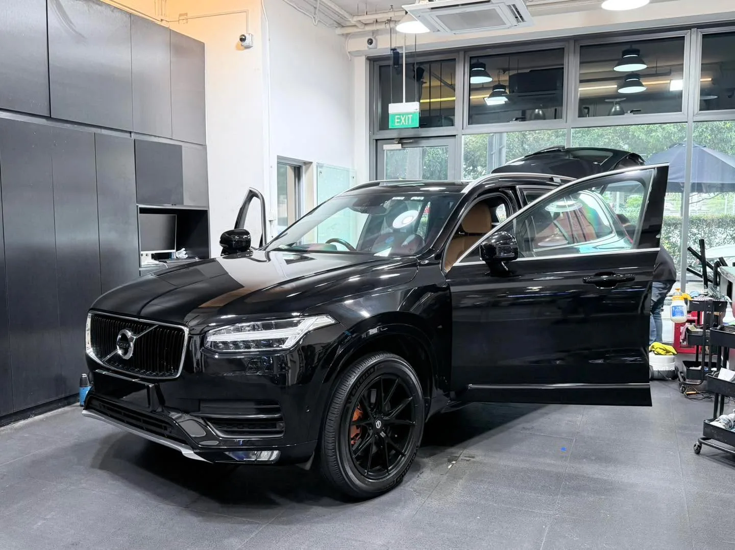 A black Volvo SUV with doors open being serviced in a workshop with tools and equipment nearby.