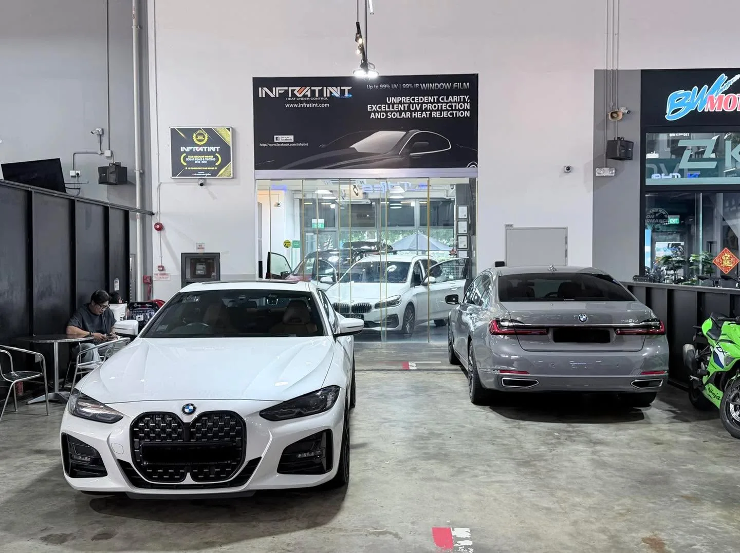 A white BMW saloon and a silver BMW saloon parked in a workshop near the storefront entrance.