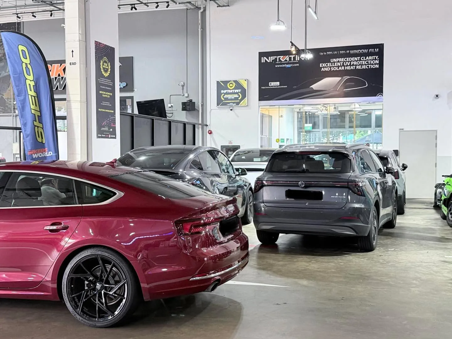 A burgundy coupe and grey SUVs in the workshop.