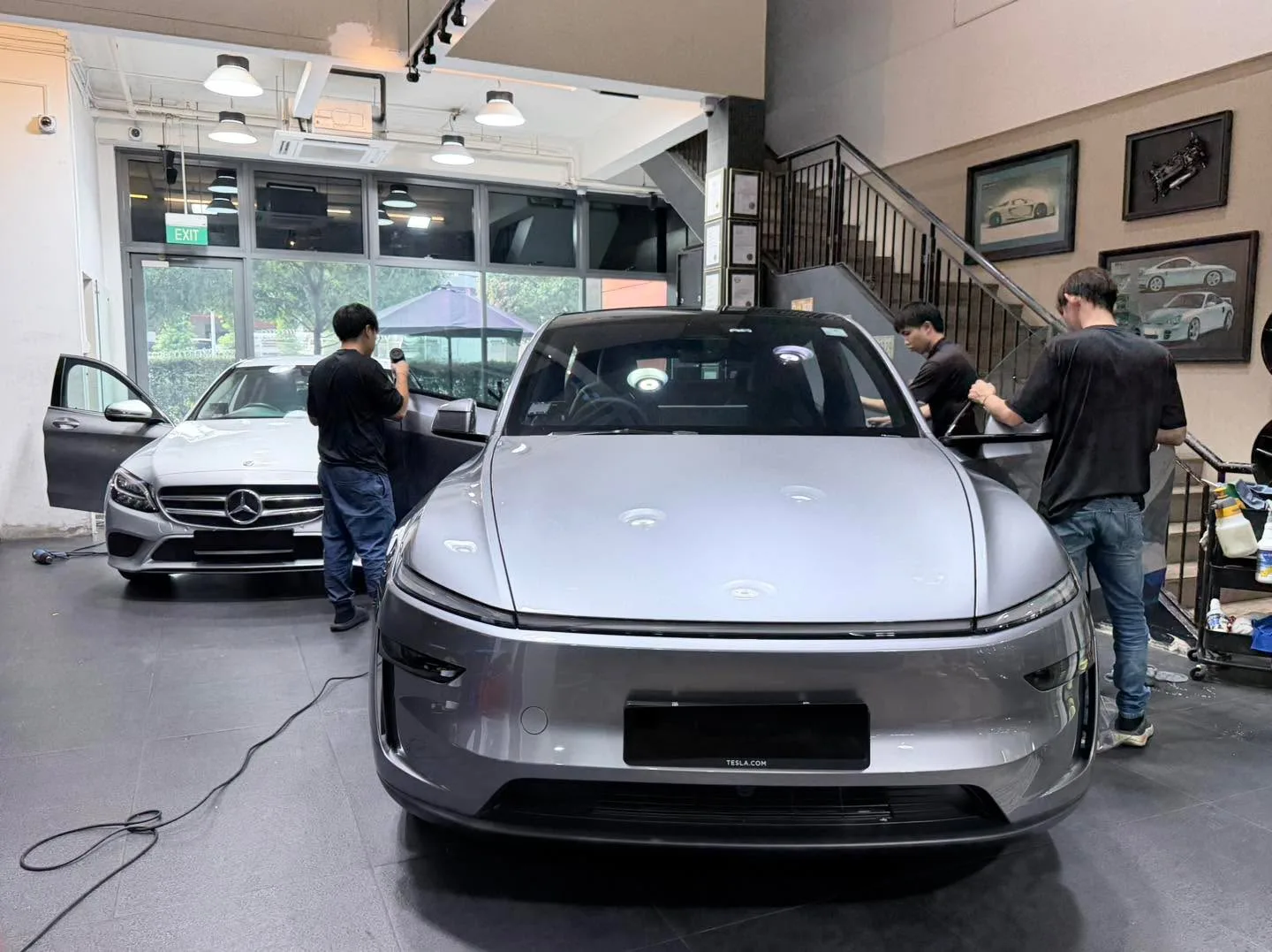 A silver sedan and grey SUVs inside the workshop with staff tinting windows.