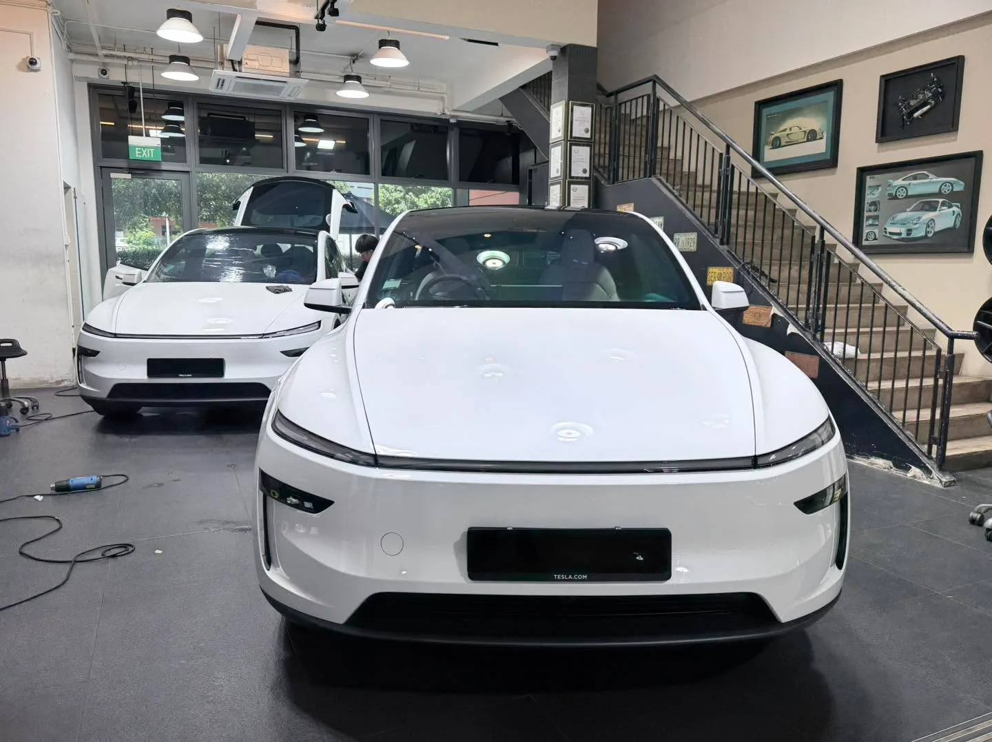 A white Tesla Model Y at the front of the workshop interior facing the camera.