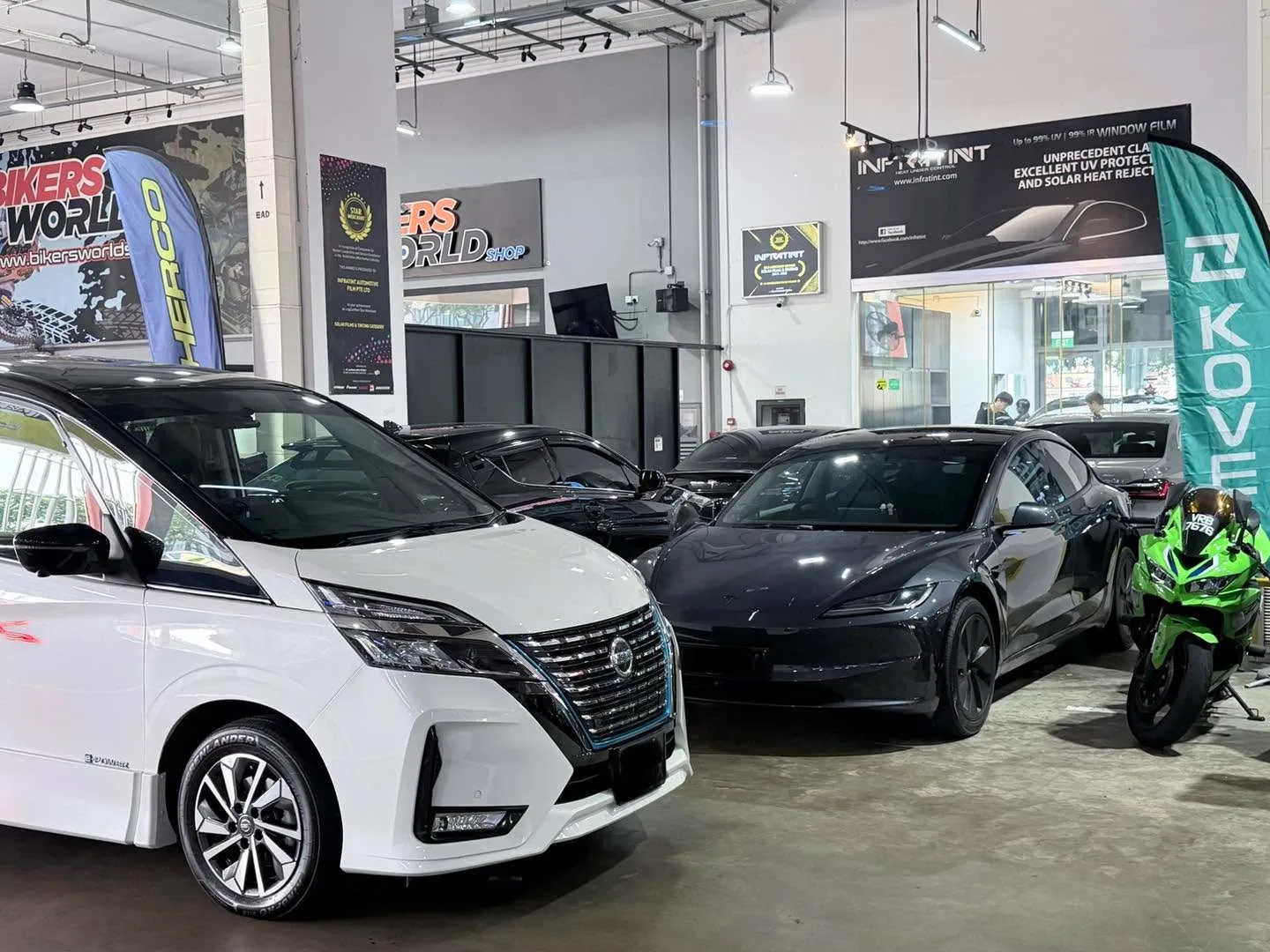 A white Nissan and black Tesla parked indoors at the workshop.
