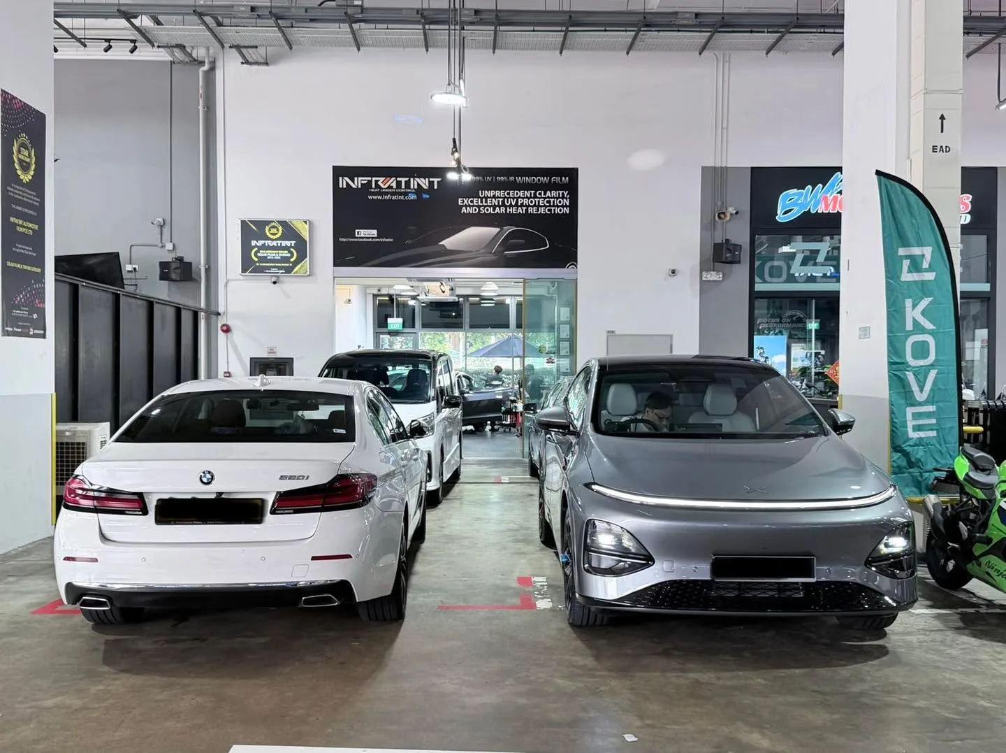 A white BMW 520 and grey Nissan Serena parked side by side indoors.