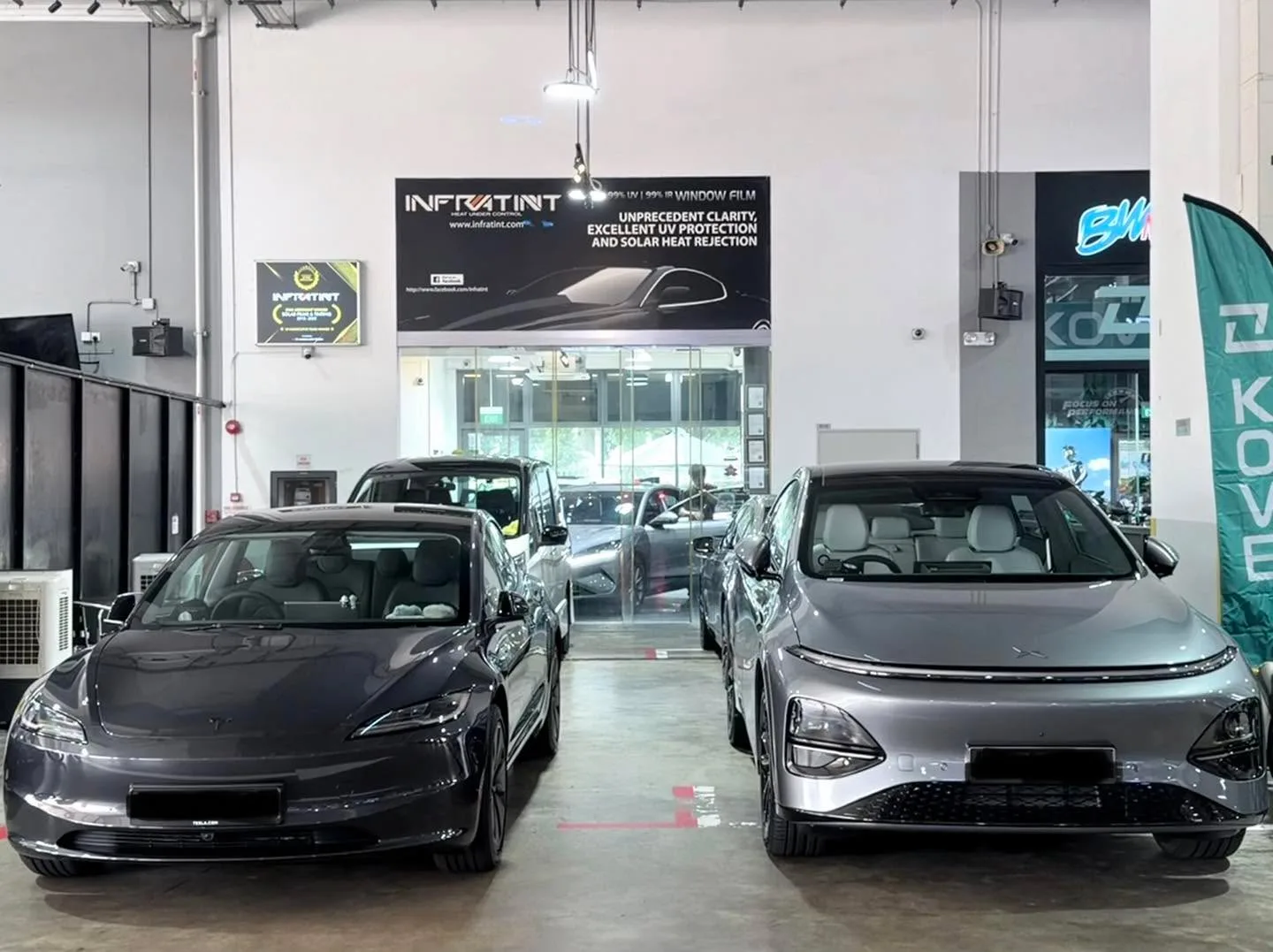A black Tesla Model 3 and grey Nissan Serena parked indoors.