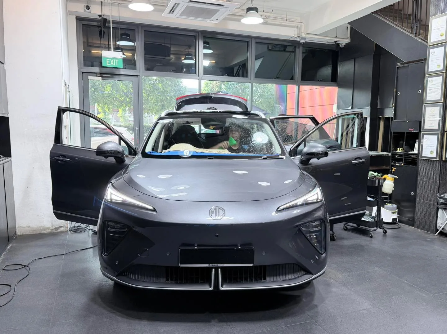 A dark grey MG hatchback with doors open during tinting work.