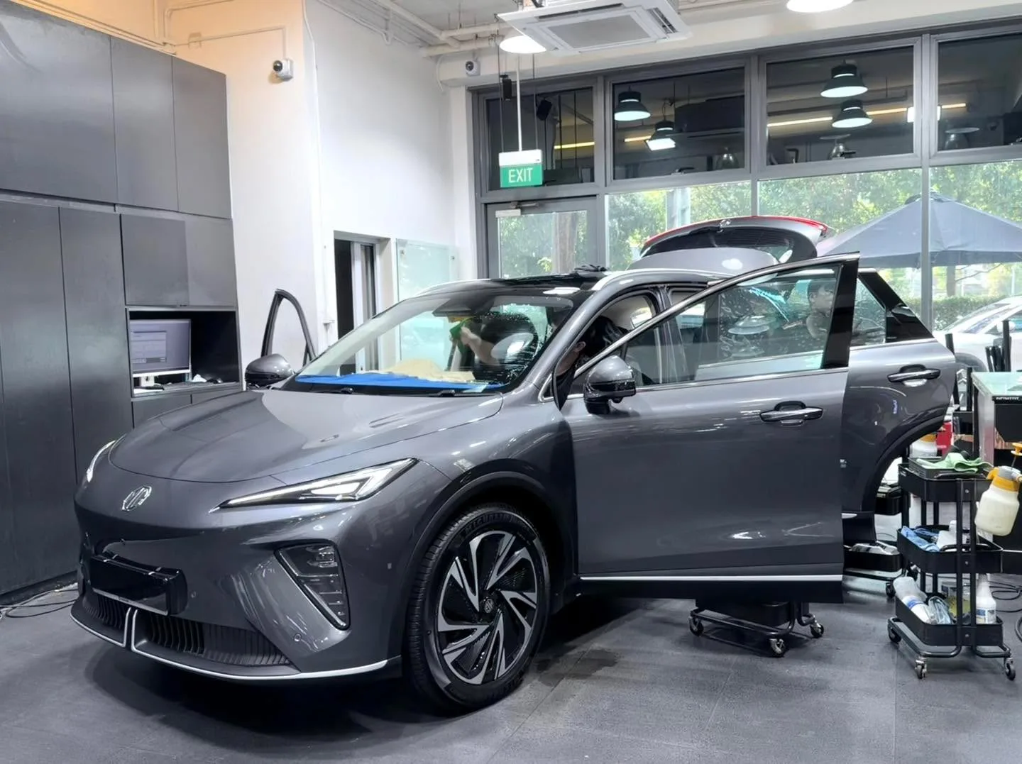 A dark grey XPENG sedan with doors open during tinting work.