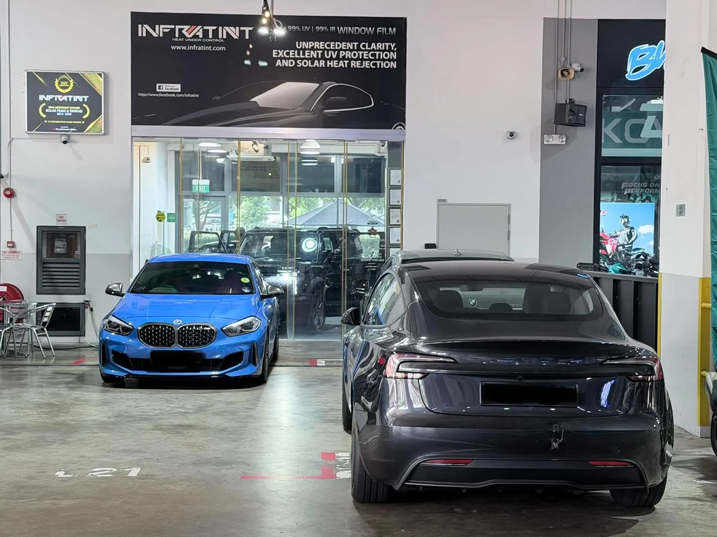 A blue BMW and a black car parked in the Infratint workshop.
