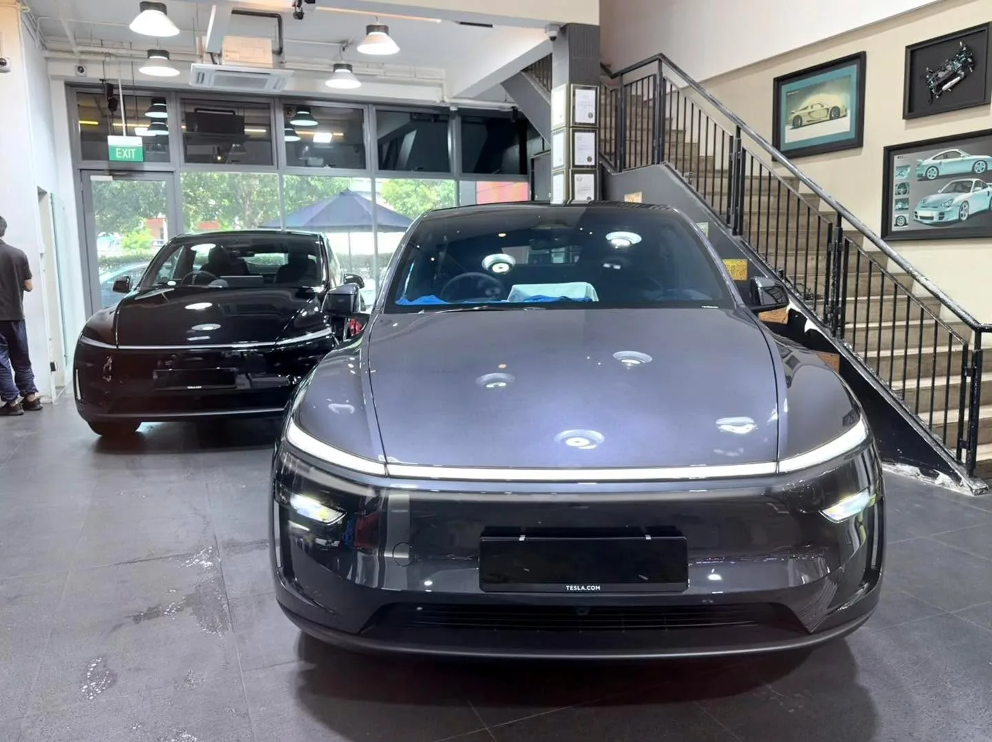 A black Tesla Model Y sedan viewed from the front in an indoor workshop space.
