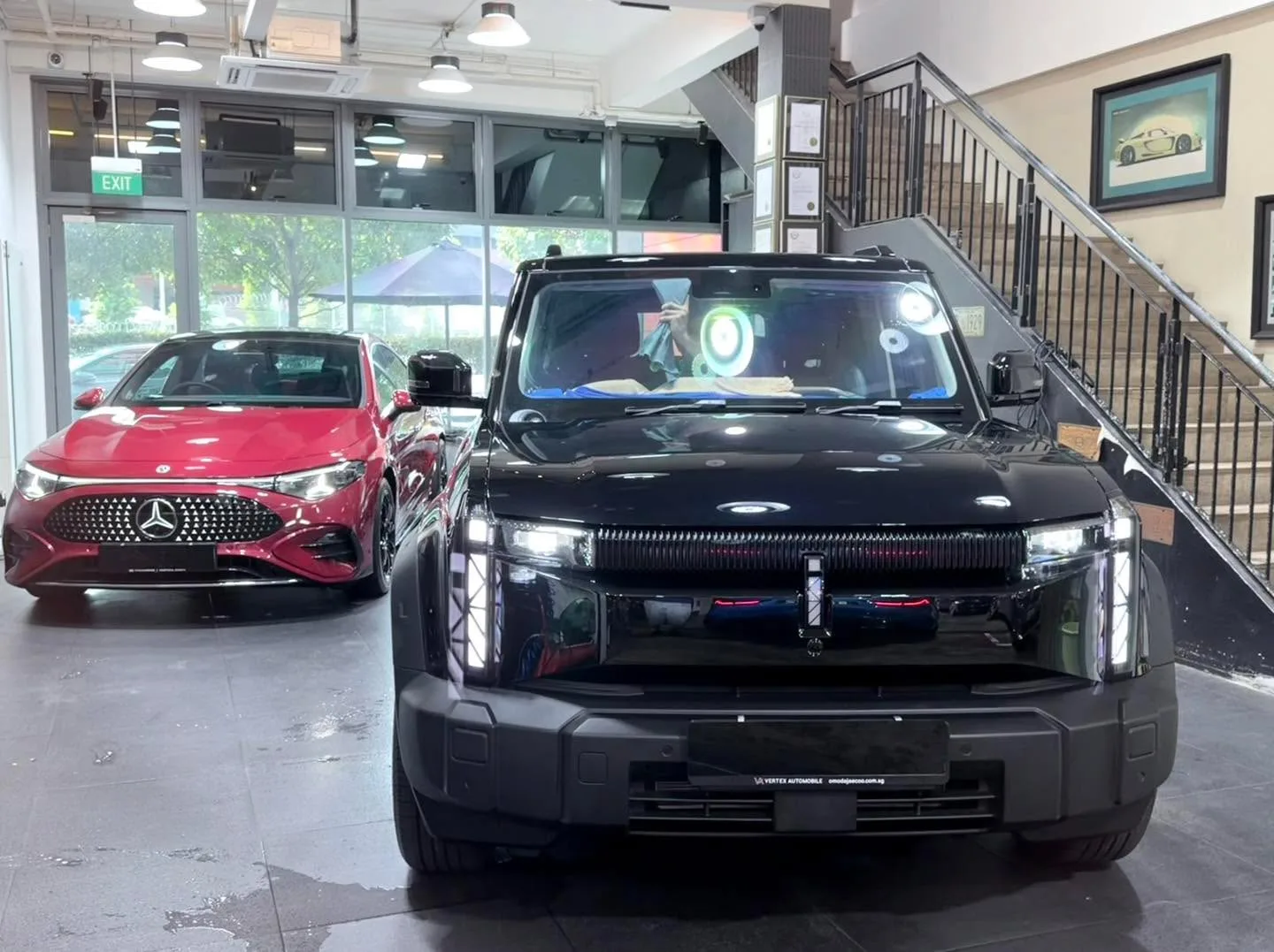 A black Tesla sedan and a red Mercedes-Benz sedan parked indoors.