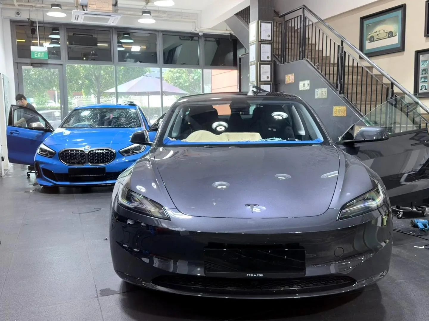 A grey Tesla Model 3 and a blue BMW 135 parked in the workshop.