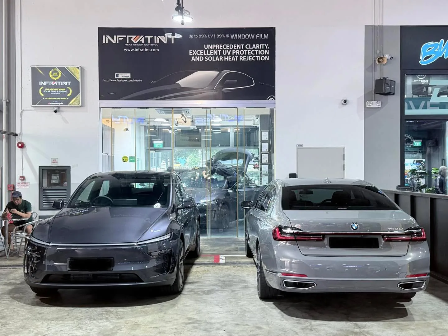 A dark-coloured electric saloon and a silver saloon parked outside the workshop front.