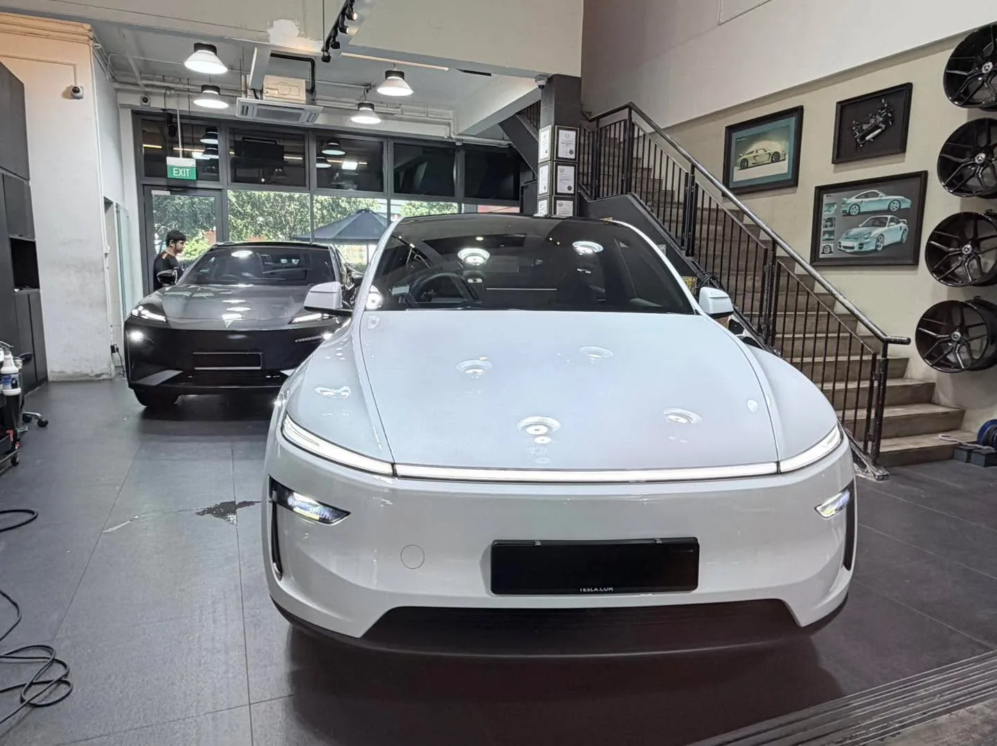 A white Tesla Model Y and a silver Mercedes saloon side by side inside the workshop.