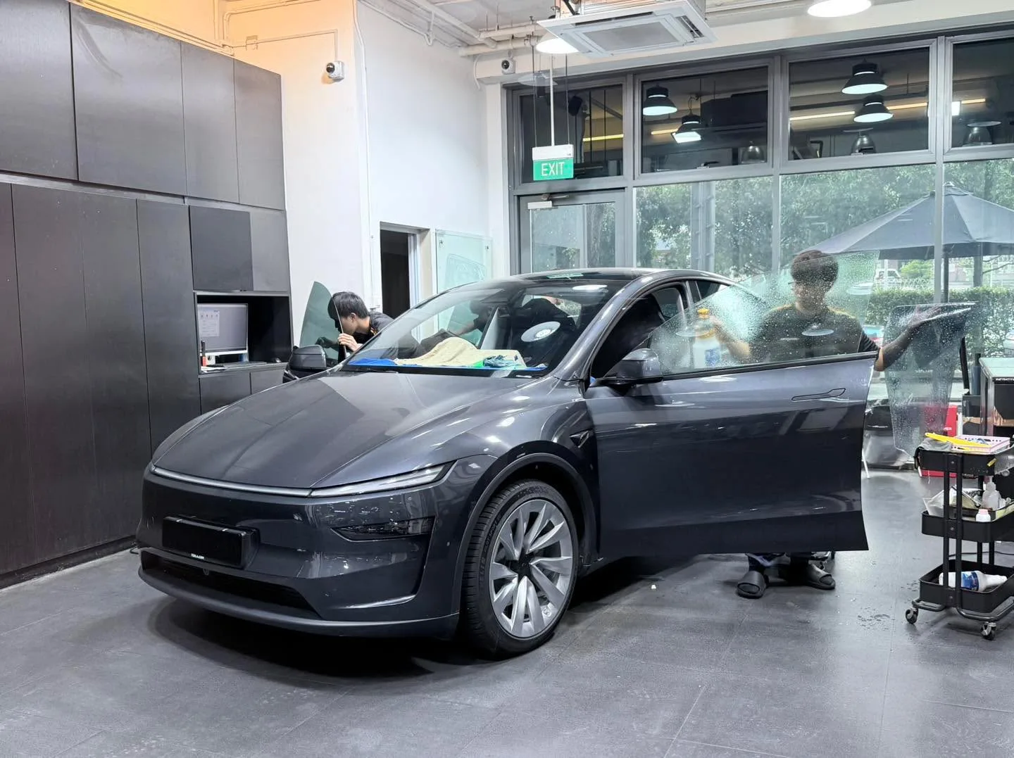 A dark-coloured Deepal S07 saloon with doors open during window tinting inside the workshop.