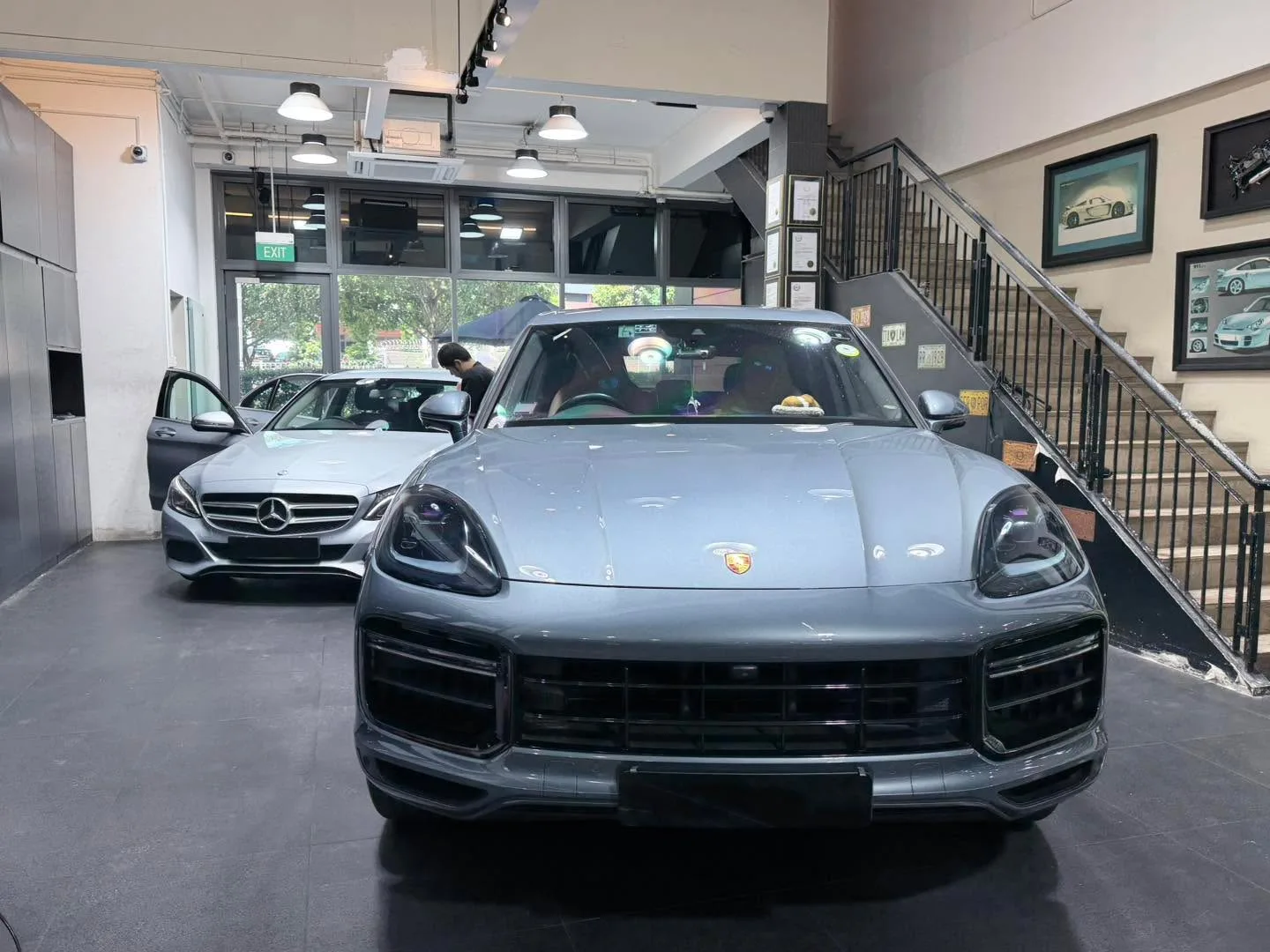 A dark grey Porsche Cayenne SUV and a light grey Mercedes-Benz sedan inside the workshop.