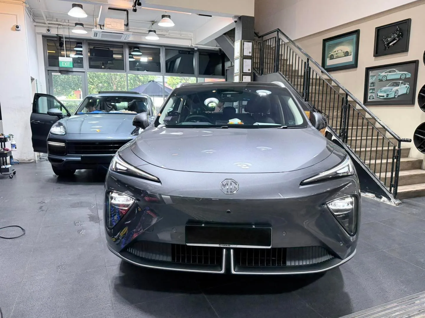 A white MG sedan and a light coloured car in the workshop interior.
