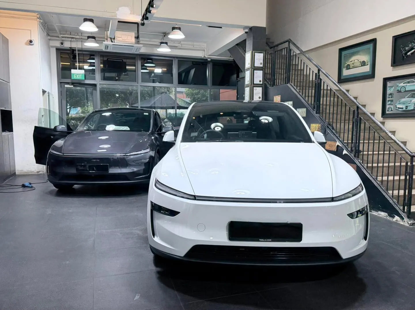 A white electric sedan and a dark car visible in the workshop.