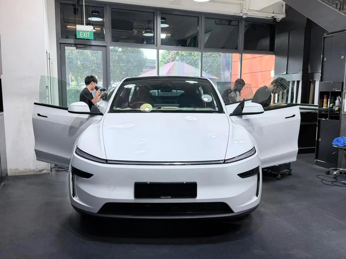 A white Tesla Model Y with both doors open as technicians work on the windows.