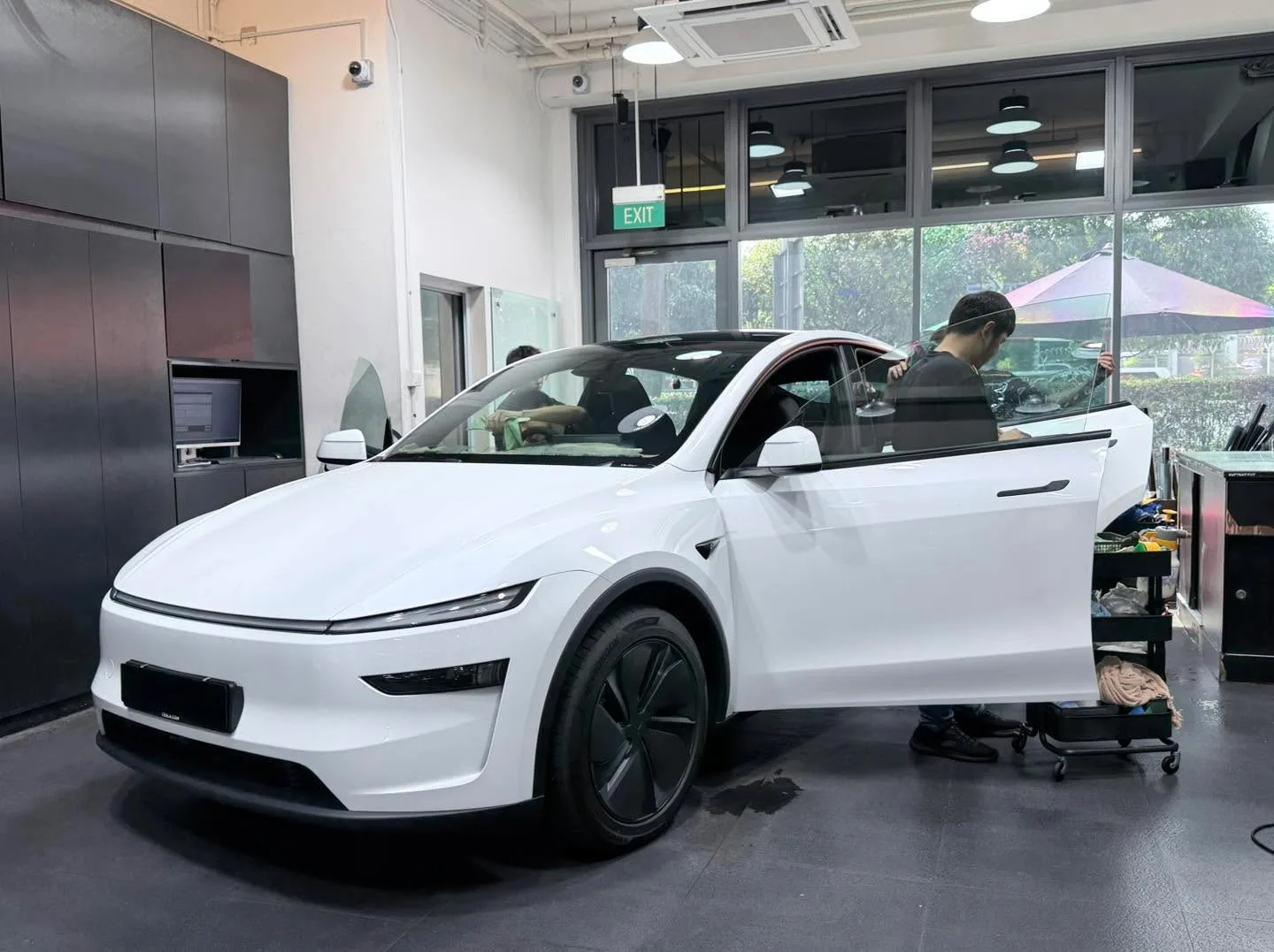 A white electric SUV viewed from the side as a technician works on the door.