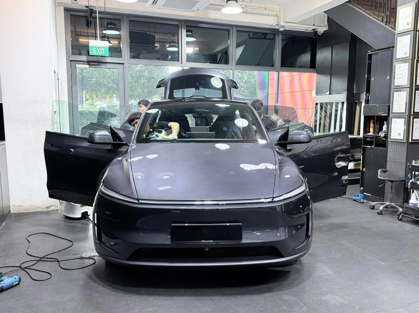 A dark grey electric sedan with doors open during window tinting work.