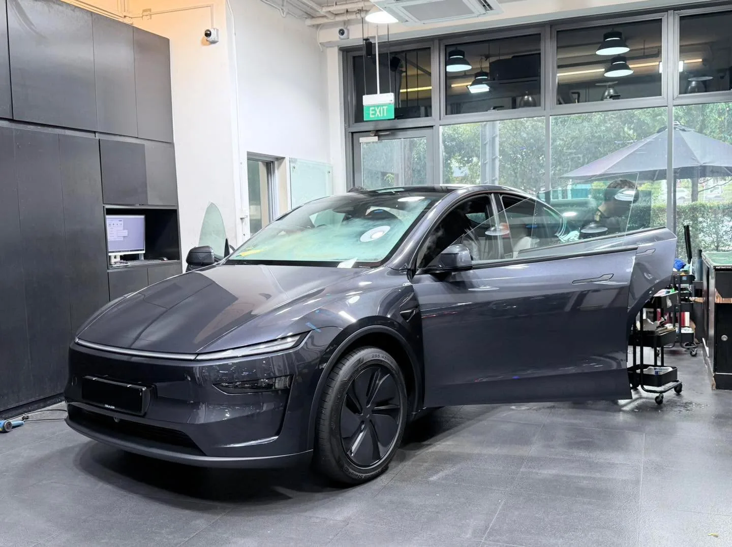 A dark Porsche Cayenne SUV with both doors open as technicians apply window film.