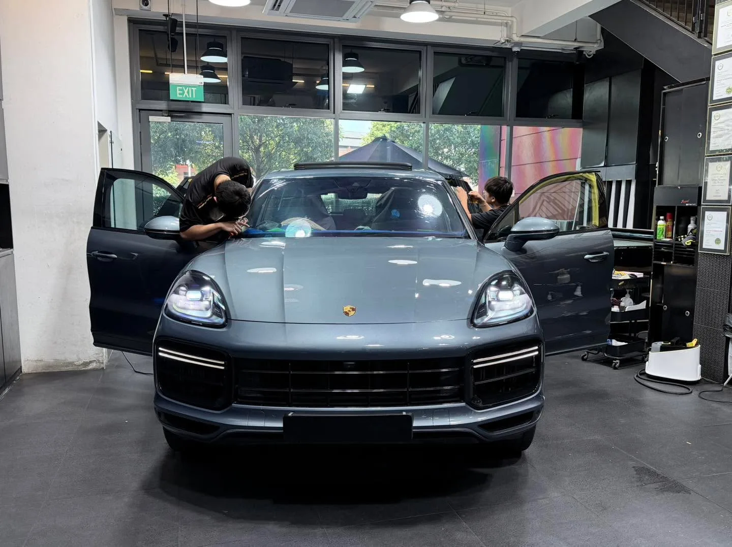 A light grey Porsche SUV with door open as technician applies window film.