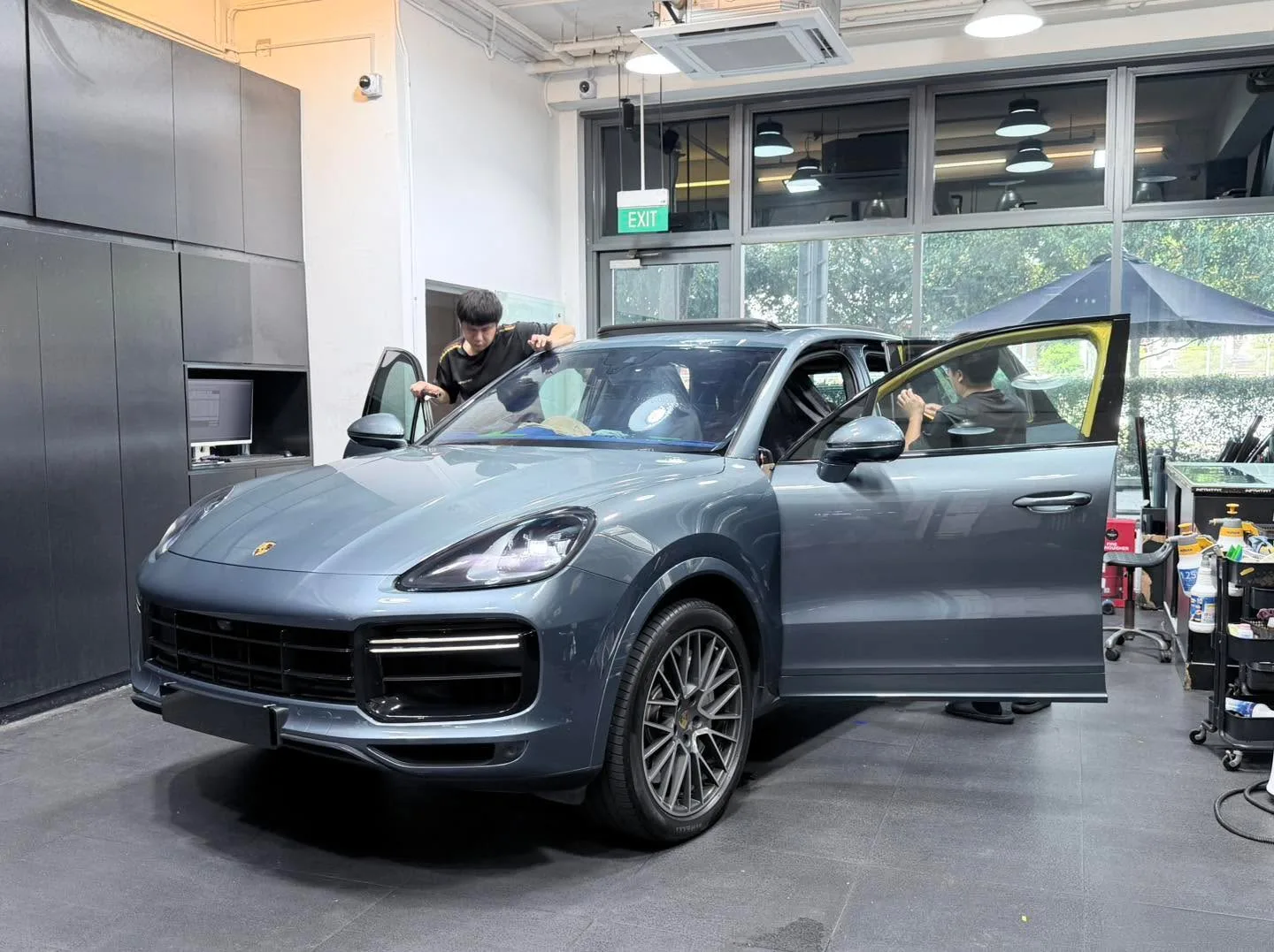 A light blue-grey Porsche Cayenne SUV with door open during window tinting work.