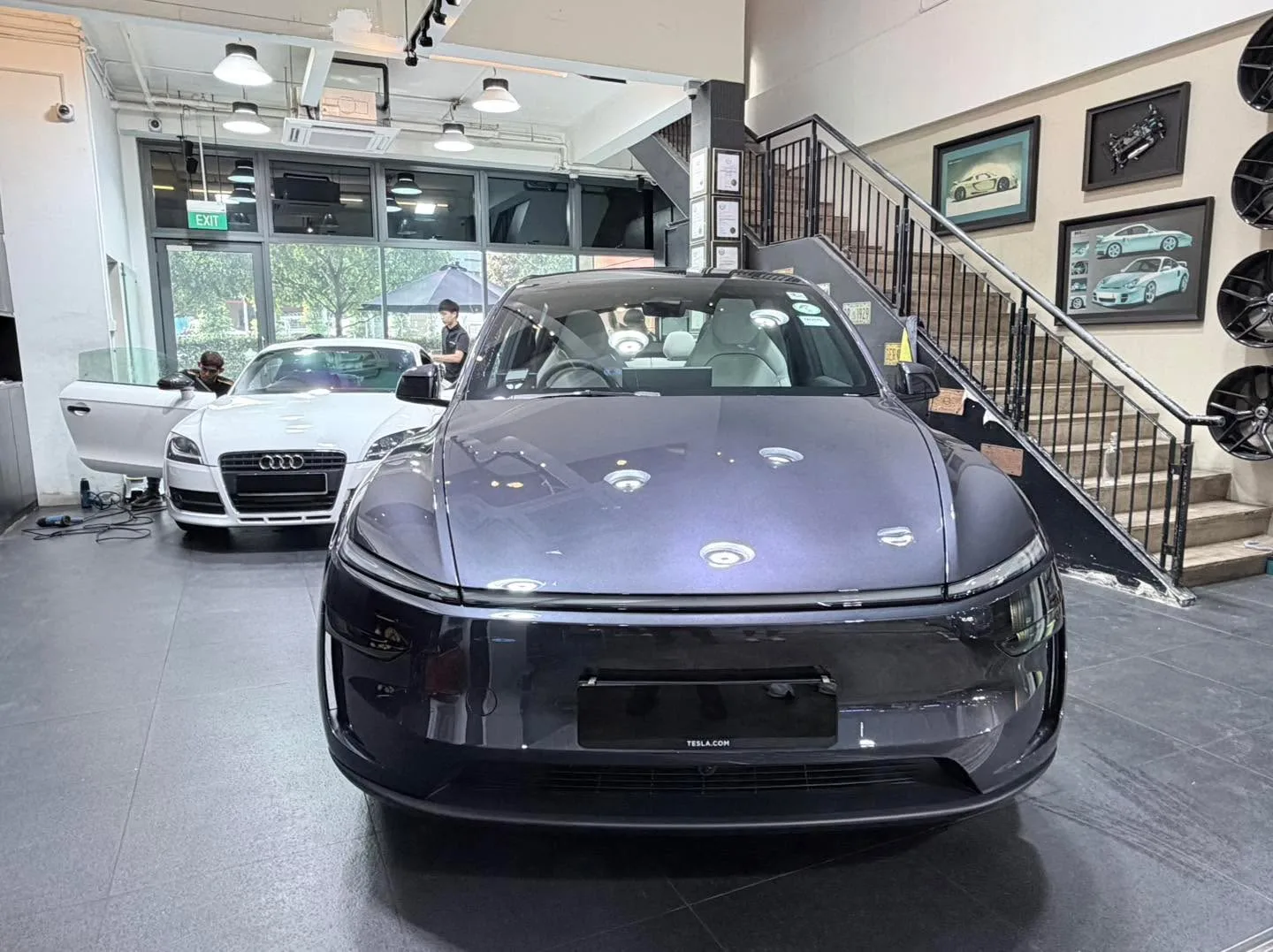 Black Tesla with prominent headlights and panel lines, viewed front-on in bright workshop.