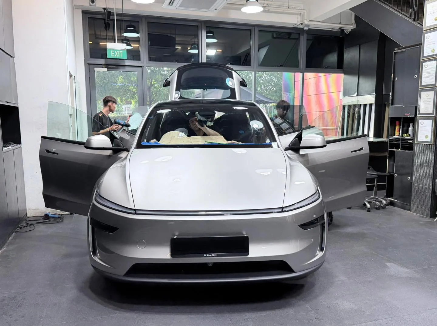 White Tesla sedan with gullwing doors open, viewed from front in workshop.