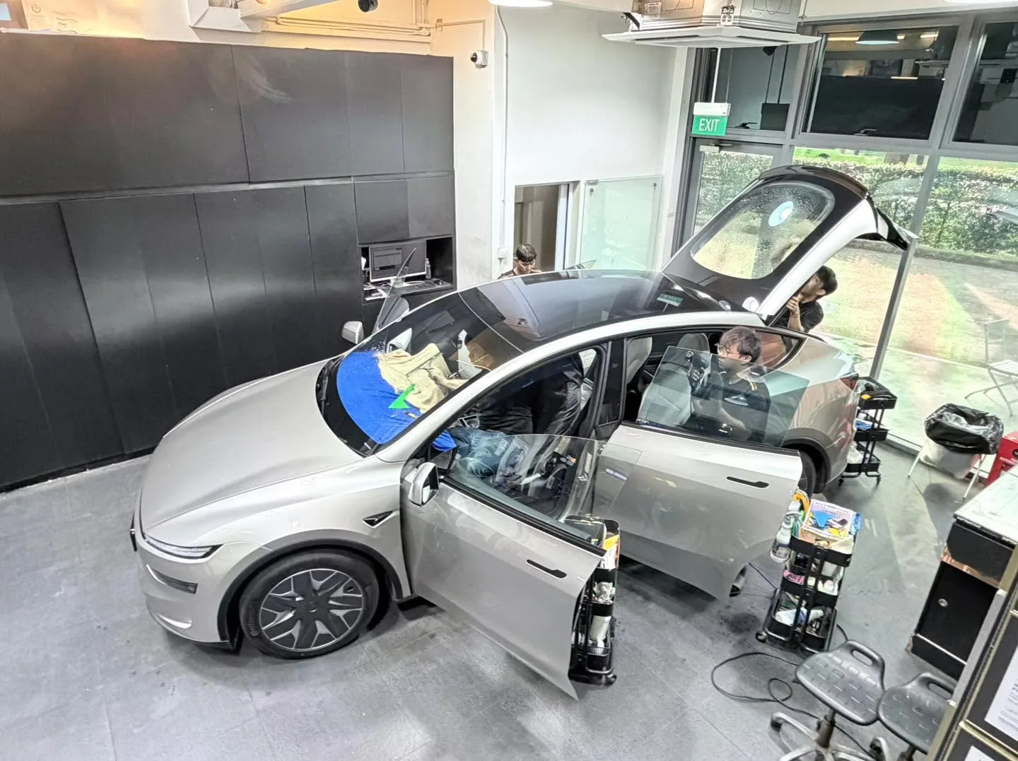 Silver and black Tesla vehicles parked in workshop with windows taped for application.