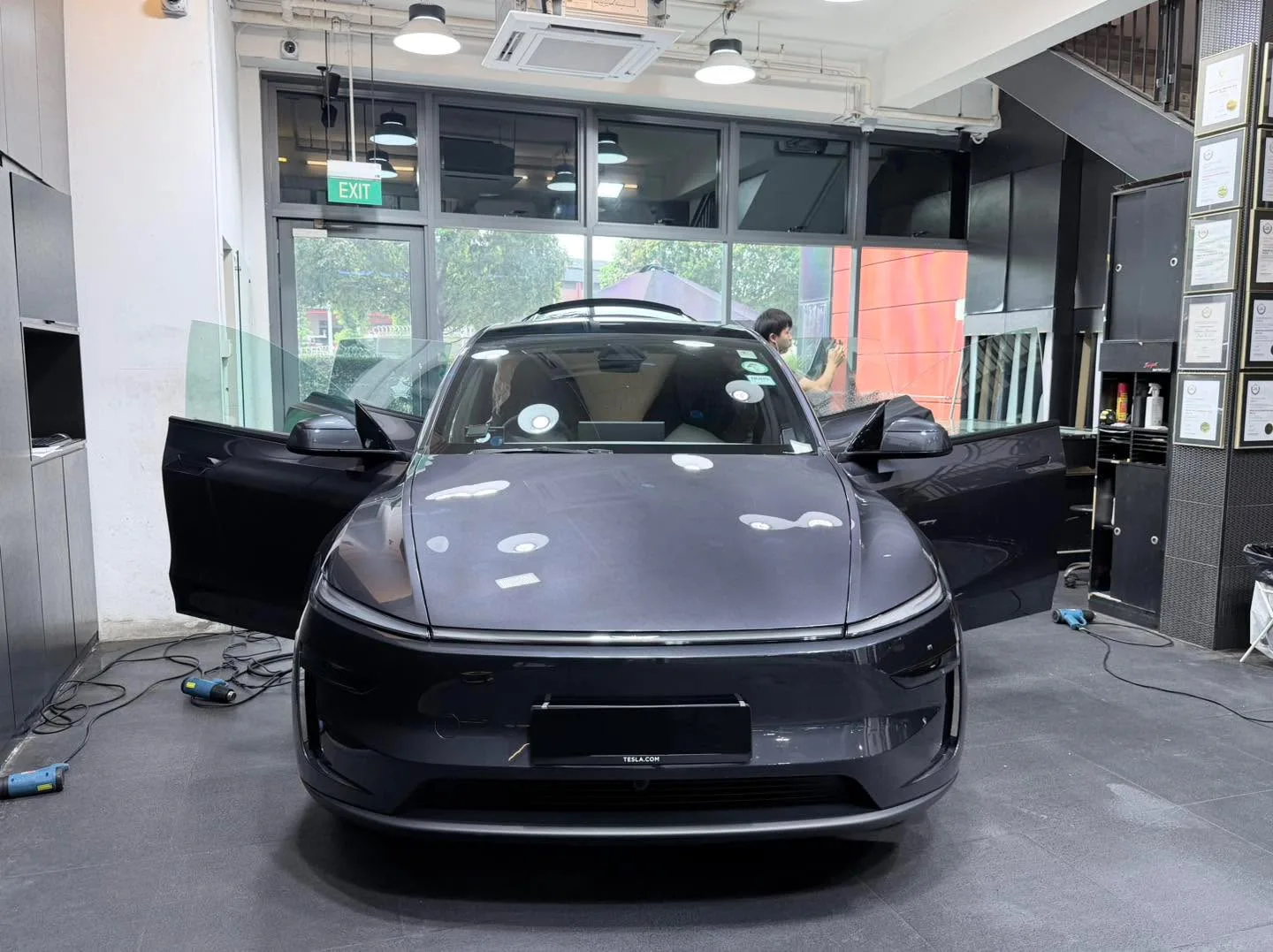Black Tesla SUV with doors open, technician visible inside workshop.