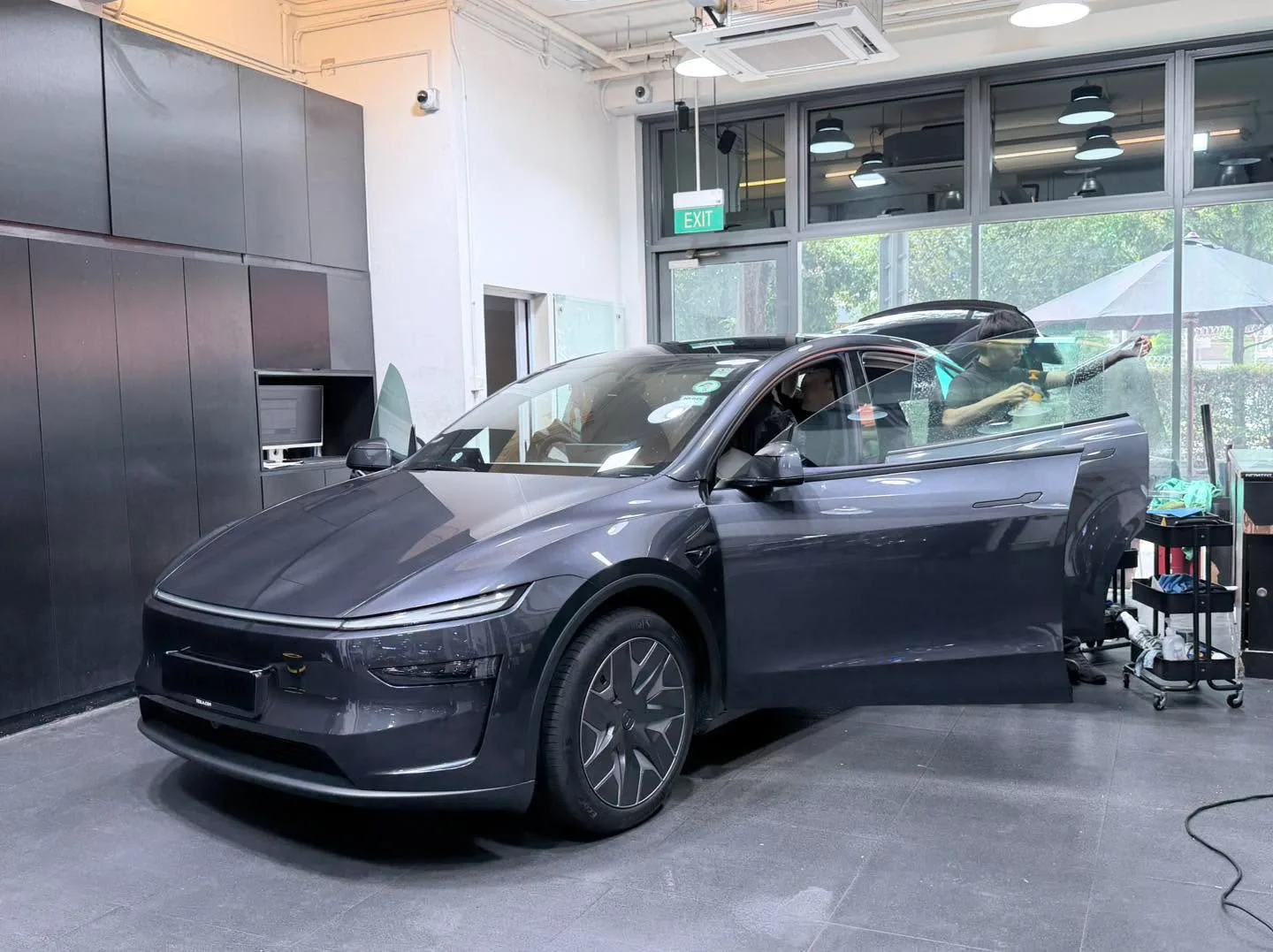 Dark blue or purple Tesla SUV with driver door open in workshop interior.