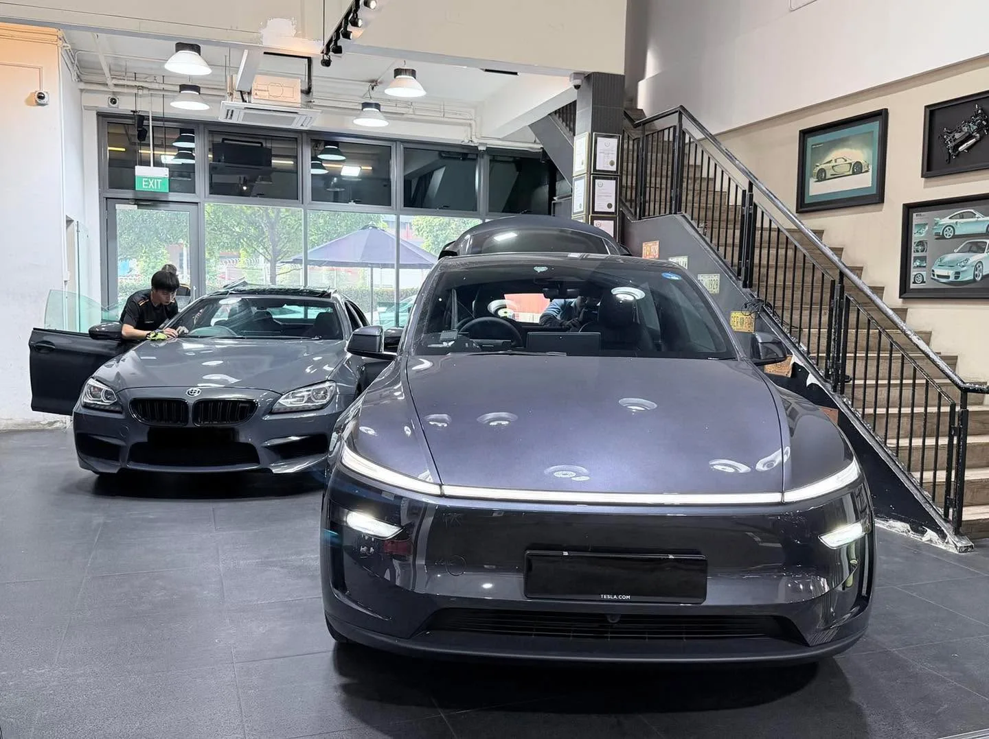 A white Tesla sedan with distinctive front design, parked indoors with a grey BMW coupe visible behind.
